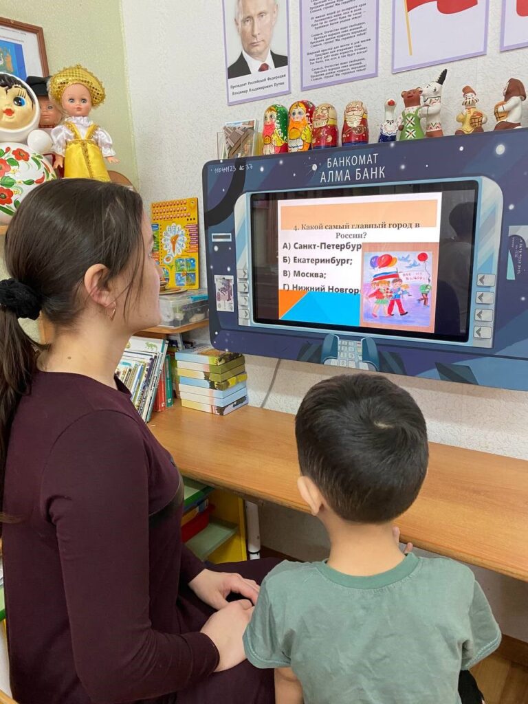 Фото 1.  Участники квест-викторины «Что мы знаем о своей стране и о выборах», проводимой в рамках Дня молодого избирателя в детском саду «Колокольчик» сидят за информационным монитором и отвечают на вопросы викторины.