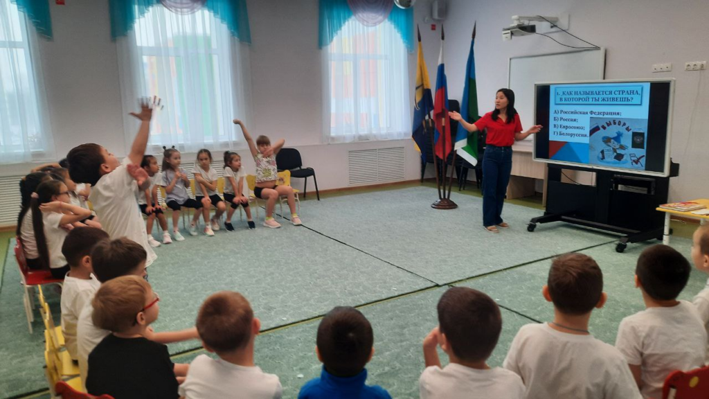 Фото 1. Участники Дня молодого избирателя в МАДОУ №8 "Огонёк" принимают участие в викторине "Что мы знаем о своей стране и выборах". На экране монитора вопрос викторины, дети подняли руки, чтобы дать на него ответ.