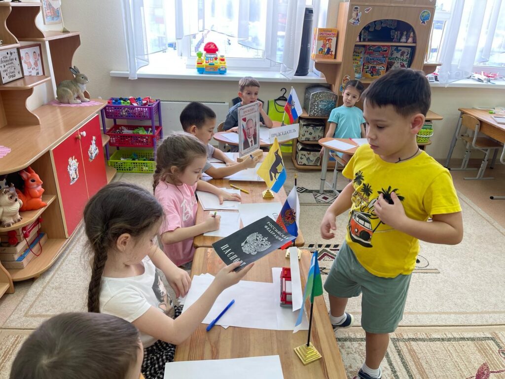 Фото 1. Участники Дня молодого избирателя в детском саду №18 «Мишутка» принимают участие в сюжетно-ролевой игре: Выборы «Президента России». Избиратель подошел к столу, где сидят члены избирательной комиссии и предъявил им паспорт гражданина РФ.  